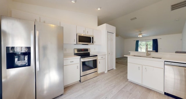 kitchen with appliances with stainless steel finishes, vaulted ceiling, light countertops, white cabinets, and a sink