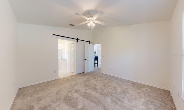 unfurnished bedroom with light colored carpet, baseboards, connected bathroom, a ceiling fan, and a barn door