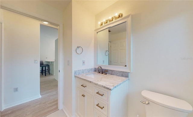 bathroom with toilet, vanity, wood finished floors, and baseboards