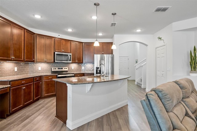 40 Oakleaf Way, Palm Coast, FL 32137 - kitchen featuring appliances with stainless steel finishes, a sink, arched walkways, light wood-type flooring, and dark stone counters