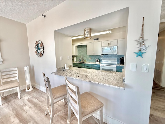 1601 N Central Ave Unit G10, Flagler Beach, FL 32136 - kitchen with white appliances, light wood-type flooring, a sink, a breakfast bar, and a textured ceiling