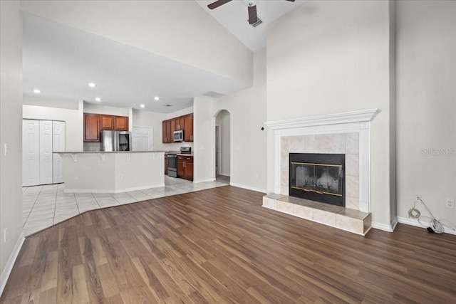 100 Point Pleasant Dr, Palm Coast, FL 32164 - unfurnished living room featuring light wood finished floors, ceiling fan, arched walkways, a tiled fireplace, and baseboards