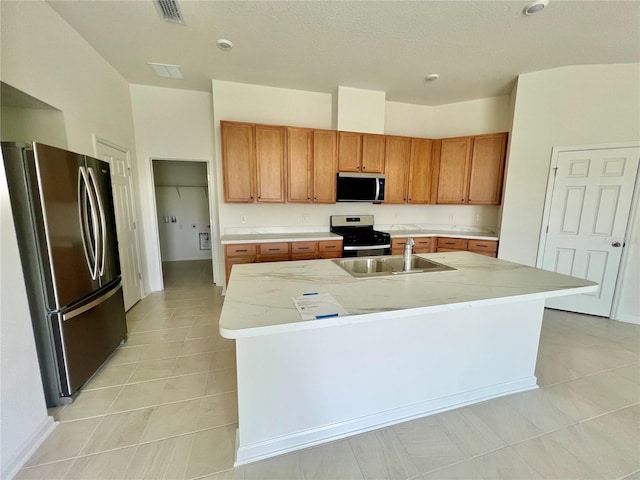 60 SW Waverly Ln, Palm Coast, FL 32164 - kitchen with stainless steel appliances, a sink, light tile patterned floors, a kitchen island with sink, and brown cabinetry
