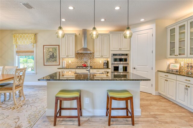 47 Hidden Treasure Dr, Palm Coast, FL 32137 - kitchen with wall chimney range hood, appliances with stainless steel finishes, a textured ceiling, a breakfast bar, and dark stone counters