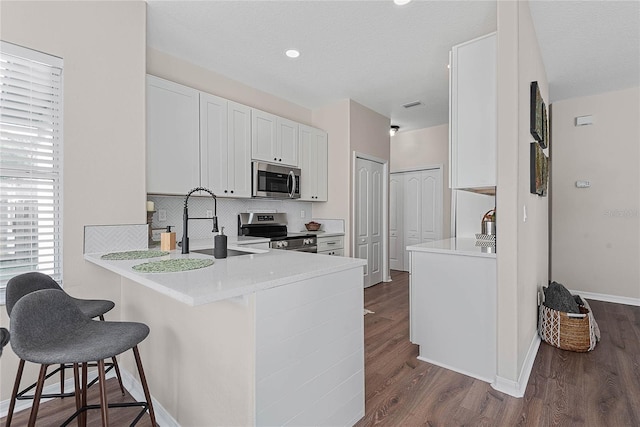 8 Zelda Ct, Palm Coast, FL 32164 - kitchen featuring stainless steel appliances, decorative backsplash, a kitchen bar, white cabinets, and dark wood-style floors