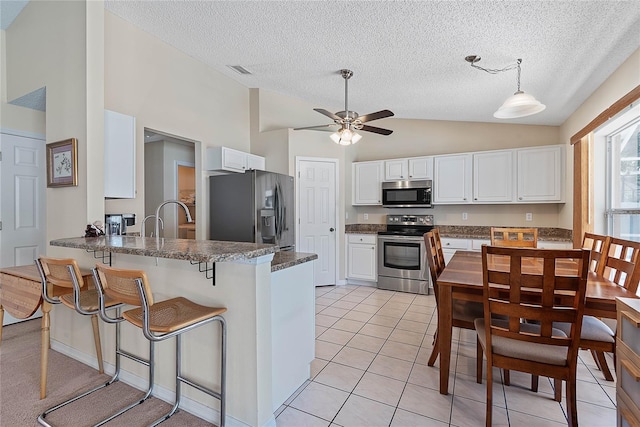 18 Royal Palm Ln, Palm Coast, FL 32164 - kitchen featuring appliances with stainless steel finishes, a peninsula, a textured ceiling, white cabinetry, and a breakfast bar area
