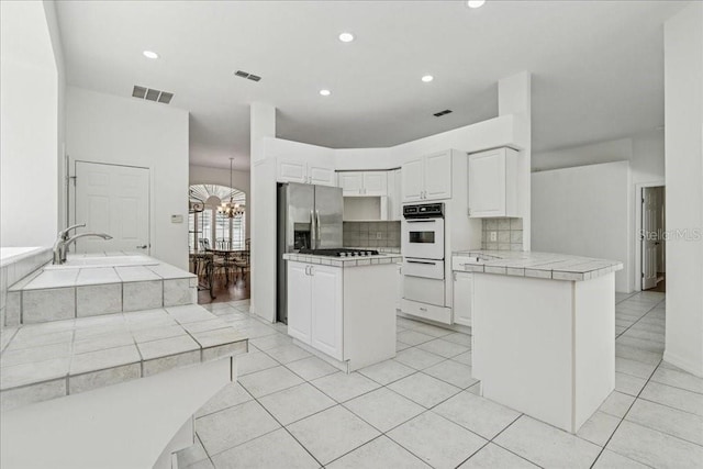 49 Ludlow Ln W, Palm Coast, FL 32137 - kitchen with white oven, a peninsula, tasteful backsplash, tile countertops, and a chandelier