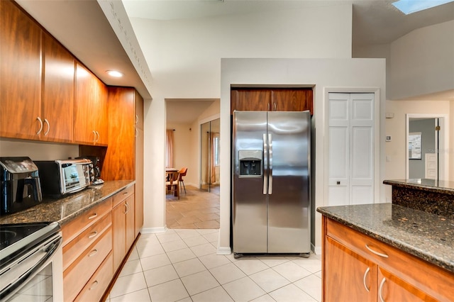 29 Cherrytree Ct, Palm Coast, FL 32137 - kitchen with stainless steel fridge with ice dispenser, light tile patterned floors, dark stone countertops, brown cabinetry, and a skylight