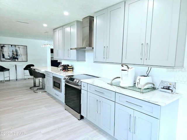 13 Sunrise Ave, Ormond Beach, FL 32176 - kitchen with wall chimney range hood, appliances with stainless steel finishes, light stone counters, light wood finished floors, and recessed lighting