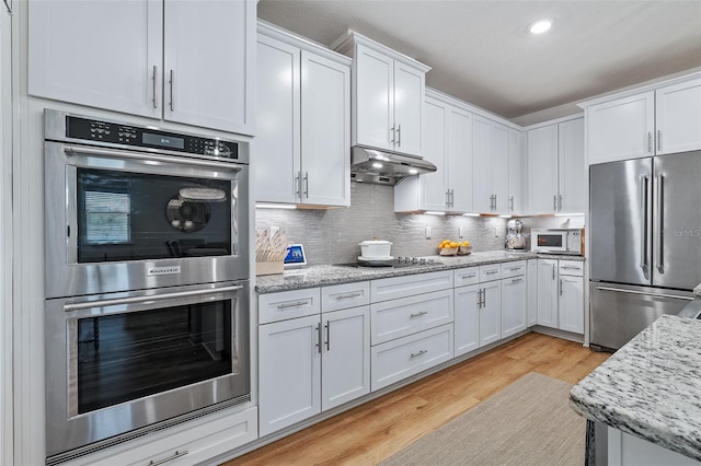 100 Las Casitas Blvd, Palm Coast, FL 32137 - kitchen with appliances with stainless steel finishes, under cabinet range hood, white cabinetry, decorative backsplash, and light wood-style flooring