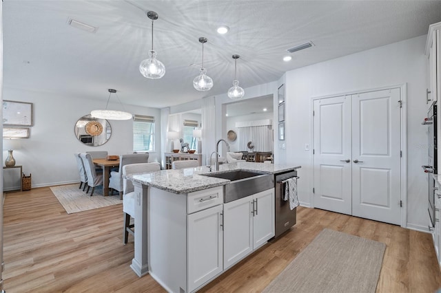 100 Las Casitas Blvd, Palm Coast, FL 32137 - kitchen featuring a sink, stainless steel dishwasher, a center island with sink, light wood-type flooring, and light stone countertops
