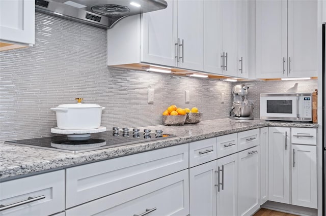 100 Las Casitas Blvd, Palm Coast, FL 32137 - kitchen featuring white microwave, ventilation hood, black electric cooktop, backsplash, and white cabinets