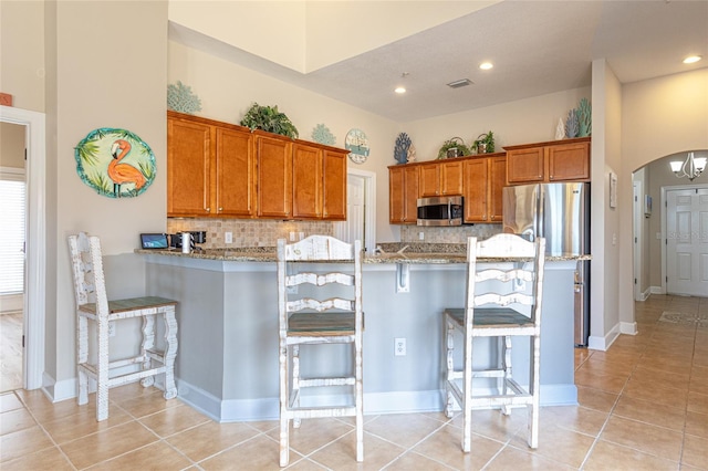 200 Bella Harbor Ct Unit 113, Palm Coast, FL 32137 - kitchen with stainless steel appliances, brown cabinetry, a breakfast bar area, arched walkways, and light stone counters