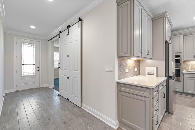 13 Las Brisas Way, Palm Coast, FL 32137 - kitchen featuring gray cabinetry, crown molding, light wood-type flooring, decorative backsplash, and a barn door
