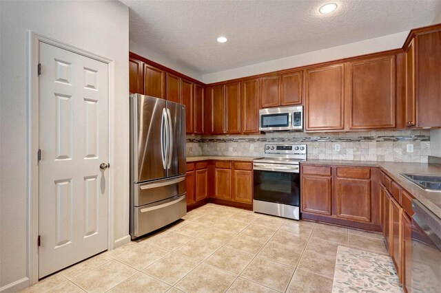 1 Rockwell Ln W, Palm Coast, FL 32164 - kitchen with stainless steel appliances, decorative backsplash, light tile patterned flooring, a textured ceiling, and brown cabinetry