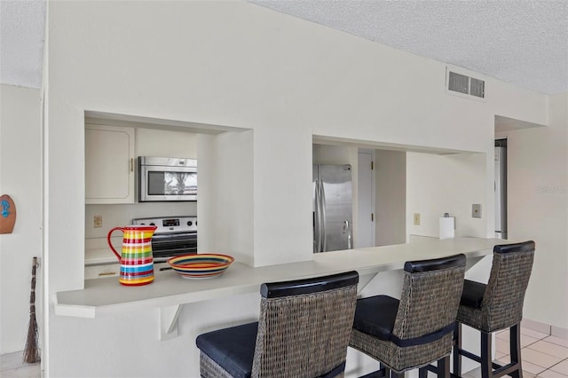 3600 S Ocean Shore Blvd Unit 222, Flagler Beach, FL 32136 - kitchen featuring appliances with stainless steel finishes, a kitchen bar, light countertops, light tile patterned floors, and a textured ceiling