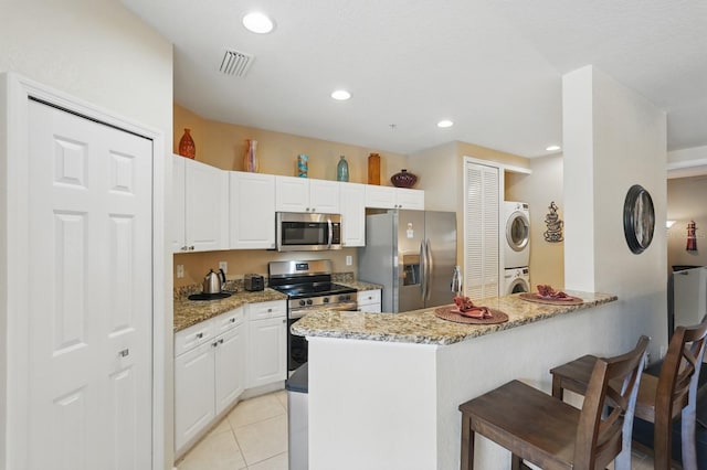 300 Via Castilla Unit 103, Saint Augustine, FL 32095 - kitchen with appliances with stainless steel finishes, stacked washer / drying machine, a kitchen bar, a peninsula, and light stone countertops