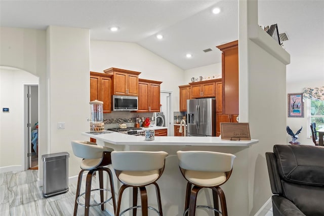 82 Ryland Dr, Palm Coast, FL 32164 - kitchen featuring appliances with stainless steel finishes, arched walkways, a kitchen bar, backsplash, and lofted ceiling