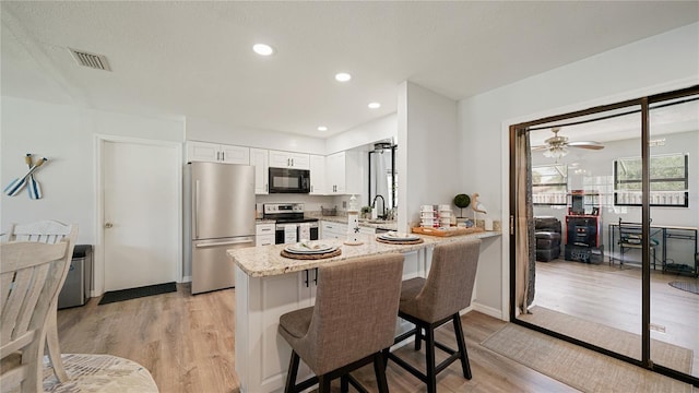 29 Firtree Ln, Palm Coast, FL 32137 - kitchen featuring appliances with stainless steel finishes, light wood-style flooring, a ceiling fan, white cabinets, and a breakfast bar