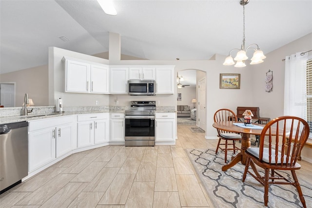 22 Post Tree Ln, Palm Coast, FL 32164 - kitchen featuring stainless steel appliances, vaulted ceiling, arched walkways, white cabinets, and light stone counters