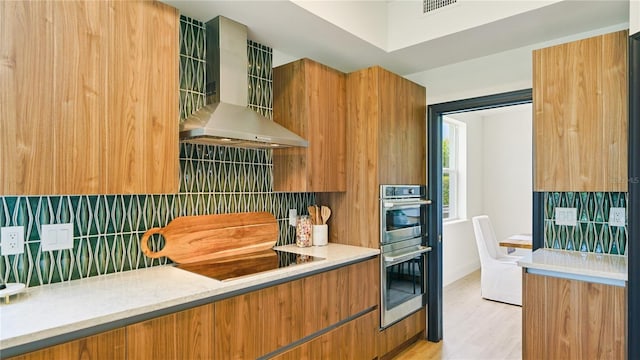 455 Riverfront Dr Unit A204, Palm Coast, FL 32137 - kitchen with wall chimney range hood, backsplash, black electric cooktop, double oven, and brown cabinetry
