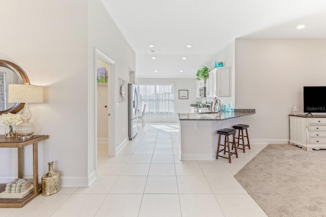 88 Rae Dr, Palm Coast, FL 32164 - kitchen with freestanding refrigerator, a kitchen breakfast bar, dark stone countertops, light tile patterned flooring, and white cabinets
