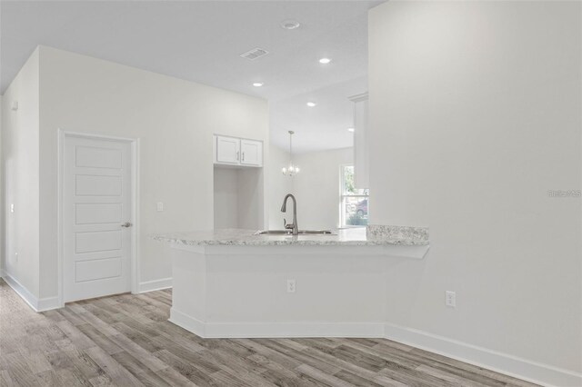 12 Wainshire Pl, Palm Coast, FL 32164 - kitchen featuring light wood-type flooring, a peninsula, recessed lighting, light stone counters, and white cabinetry