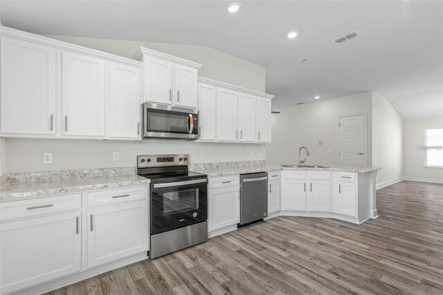 12 Wainshire Pl, Palm Coast, FL 32164 - kitchen with stainless steel appliances, a peninsula, light wood-style flooring, white cabinets, and vaulted ceiling