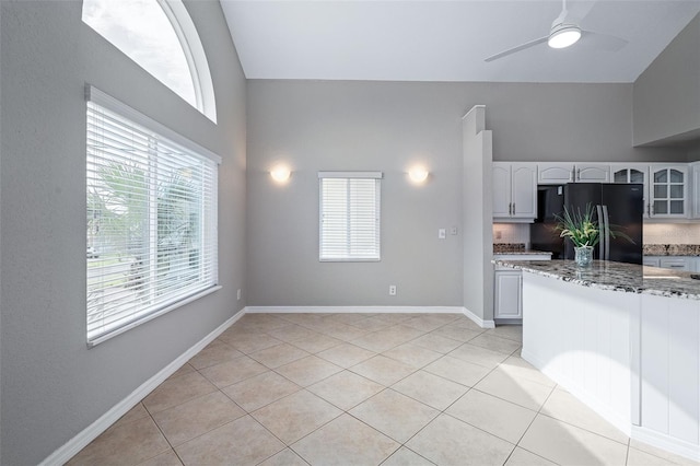 1115 N Central Ave, Flagler Beach, FL 32136 - kitchen featuring freestanding refrigerator, light stone counters, light tile patterned floors, glass insert cabinets, and a ceiling fan