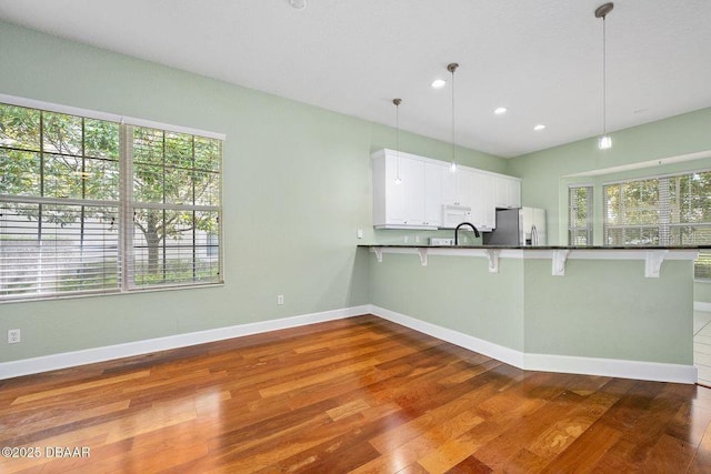 3132 Connemara Dr, Ormond Beach, FL 32174 - kitchen with stainless steel fridge, dark countertops, dark wood-style floors, a kitchen bar, and recessed lighting