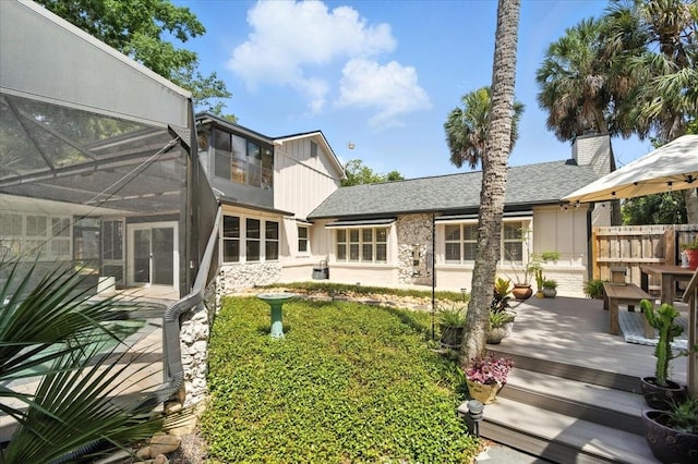 1108 Shockney Dr, Ormond Beach, FL 32174 - back of property with a deck, glass enclosure, stone siding, a shingled roof, and a chimney