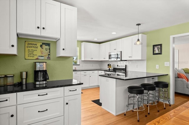1026 Bel Aire Dr, Daytona Beach, FL 32118 - kitchen featuring stainless steel appliances, white cabinets, light wood finished floors, a peninsula, and decorative backsplash