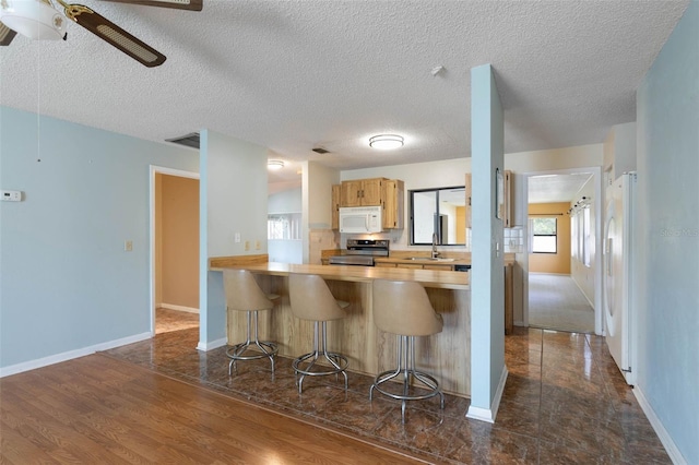 1 Wilson Pl, Palm Coast, FL 32164 - kitchen with white appliances, a ceiling fan, a kitchen bar, light countertops, and a textured ceiling