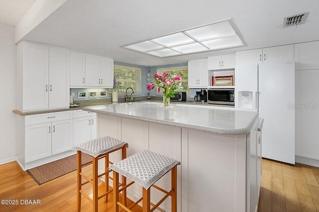 1108 Northside Dr, Ormond Beach, FL 32174 - kitchen featuring stainless steel microwave, white refrigerator with ice dispenser, light wood-type flooring, white cabinetry, and a textured ceiling