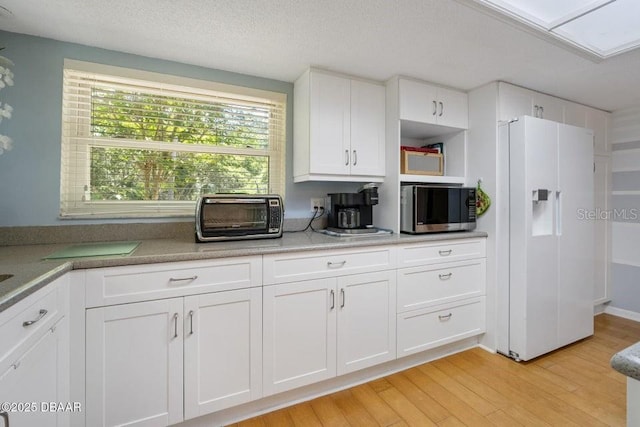 1108 Northside Dr, Ormond Beach, FL 32174 - kitchen featuring white fridge with ice dispenser, stainless steel microwave, light wood finished floors, white cabinetry, and light countertops