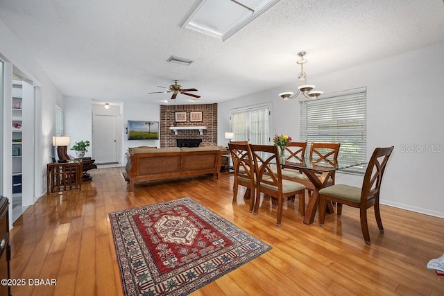 1108 Northside Dr, Ormond Beach, FL 32174 - dining area with a fireplace, light wood-style flooring, a textured ceiling, and a ceiling fan
