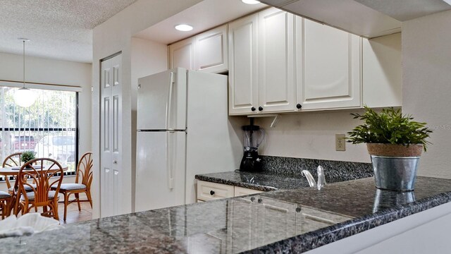 4655 46th Street Ct W Unit 101, Bradenton, FL 34210 - kitchen featuring freestanding refrigerator, white cabinets, dark stone counters, a textured ceiling, and decorative light fixtures