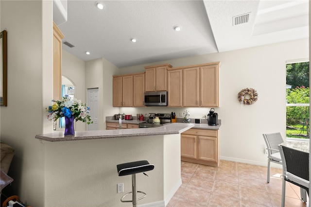 143 W Waterside Pkwy, Palm Coast, FL 32137 - kitchen with light brown cabinetry, appliances with stainless steel finishes, a peninsula, a breakfast bar area, and light tile patterned floors