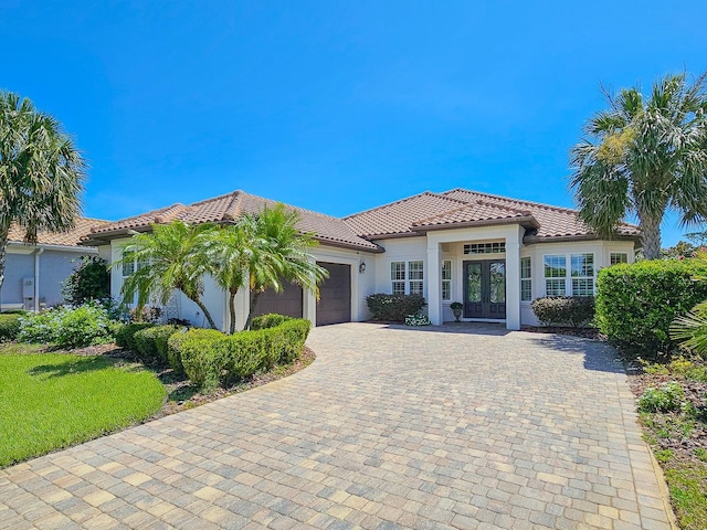 145 Heron Dr, Palm Coast, FL 32137 - mediterranean / spanish house featuring french doors, a tiled roof, an attached garage, stucco siding, and decorative driveway