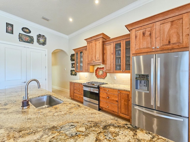 145 Heron Dr, Palm Coast, FL 32137 - kitchen featuring appliances with stainless steel finishes, brown cabinets, arched walkways, ornamental molding, and light stone countertops