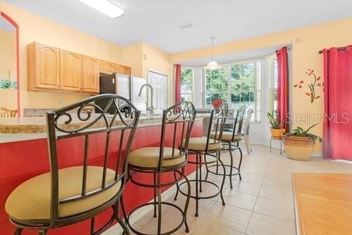 7 Flint Pl, Palm Coast, FL 32137 - kitchen with light brown cabinets, a breakfast bar area, light tile patterned floors, freestanding refrigerator, and light countertops