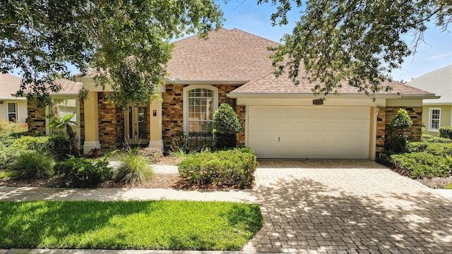 67 Lagare St, Palm Coast, FL 32137 - view of front of house featuring a garage, stone siding, decorative driveway, and roof with shingles