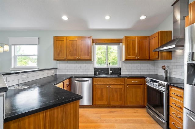 19 Bay Dr, Palm Coast, FL 32137 - kitchen with wall chimney range hood, appliances with stainless steel finishes, brown cabinets, light wood finished floors, and a peninsula