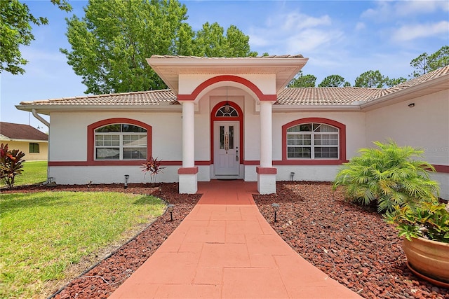 54 Pine Grove Dr, Palm Coast, FL 32164 - view of exterior entry featuring a tiled roof, a lawn, and stucco siding