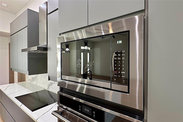 179 Eric Dr, Palm Coast, FL 32164 - detailed view of wall chimney exhaust hood, gray cabinetry, decorative backsplash, stainless steel appliances, and modern cabinets