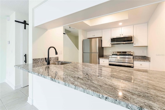 3630 S Central Ave, Flagler Beach, FL 32136 - kitchen featuring stainless steel appliances, a barn door, light stone counters, light tile patterned floors, and white cabinetry