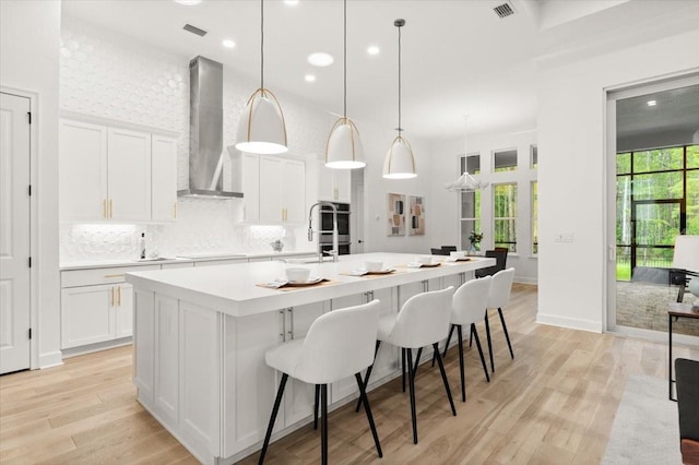 476 Stirling Bridge Dr, Ormond Beach, FL 32174 - kitchen featuring wall chimney exhaust hood, a spacious island, light countertops, white cabinets, and light wood-style flooring
