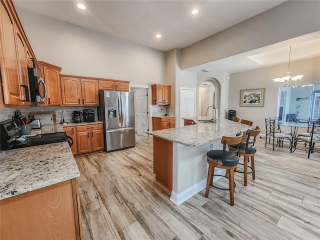 8 Wiltshire Pl, Palm Coast, FL 32164 - kitchen featuring black range with electric stovetop, stainless steel refrigerator with ice dispenser, brown cabinetry, a breakfast bar, and backsplash