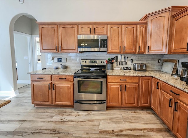 8 Wiltshire Pl, Palm Coast, FL 32164 - kitchen featuring appliances with stainless steel finishes, tasteful backsplash, arched walkways, light stone countertops, and light wood-style flooring