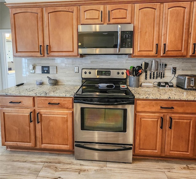 8 Wiltshire Pl, Palm Coast, FL 32164 - kitchen with appliances with stainless steel finishes, decorative backsplash, light stone counters, light wood-type flooring, and brown cabinetry